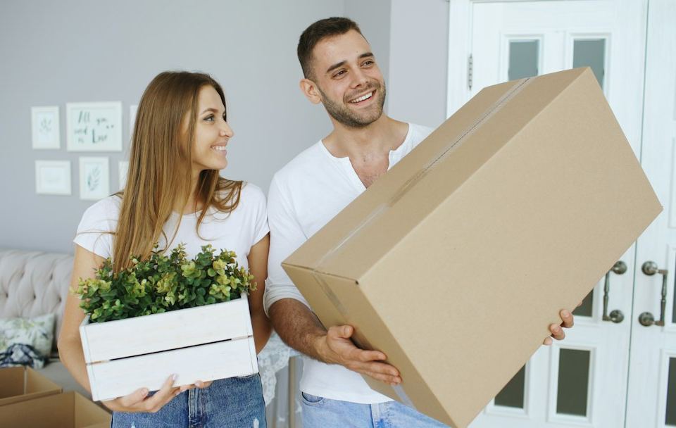 Couple carrying a large box and a plant
